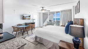 Een hotelkamer met een bed, een bureau, een stoel, een televisie, een balkon met uitzicht en een plafondventilator.