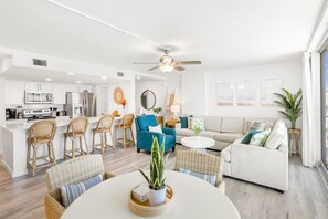 A modern kitchen with white cabinets, stainless steel appliances, and a dining area with wicker furniture and a central plant.