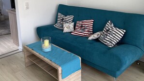 Un canapé de couleur turquoise agrémenté de coussins à rayures et à motifs, un porte-bougie en verre posé sur une petite table en bois, et une carte du monde accrochée au mur.