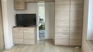 Une pièce avec un téléviseur posé sur un meuble en bois, une armoire et une porte donnant sur une autre pièce.