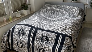 Une chambre à coucher avec un lit, deux fenêtres équipées de stores, un radiateur et une petite plante en pot.