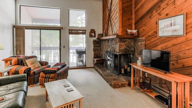 A cozy living room with a stone fireplace, a television, and a sofa with striped cushions. - Cozy Mountain Condo w/Outdoor Heated Pool Access (Fraser)