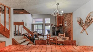 A spacious living area with a wooden staircase, a dining table set for four, and a fireplace. - Cozy Mountain Condo w/Outdoor Heated Pool Access (Fraser)