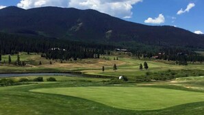 A golf course with a mountain backdrop, a lake, and a clear sky. - Cozy Mountain Condo w/Outdoor Heated Pool Access (Fraser)
