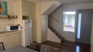A compact kitchen with a microwave, refrigerator, and a dining area with a table and chairs. A staircase leads to a balcony with a door and a window. - Beaton's Beach Front Studio - Inverloch (Inverloch)
