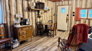 Une pièce chaleureuse avec des murs en bois, une table à manger, des chaises, un coin café et un fauteuil à bascule.