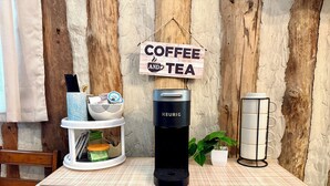 Un comptoir de cuisine avec une machine à café, une pancarte indiquant « CAFÉ ET THÉ », une plante et un porte-tasses.
