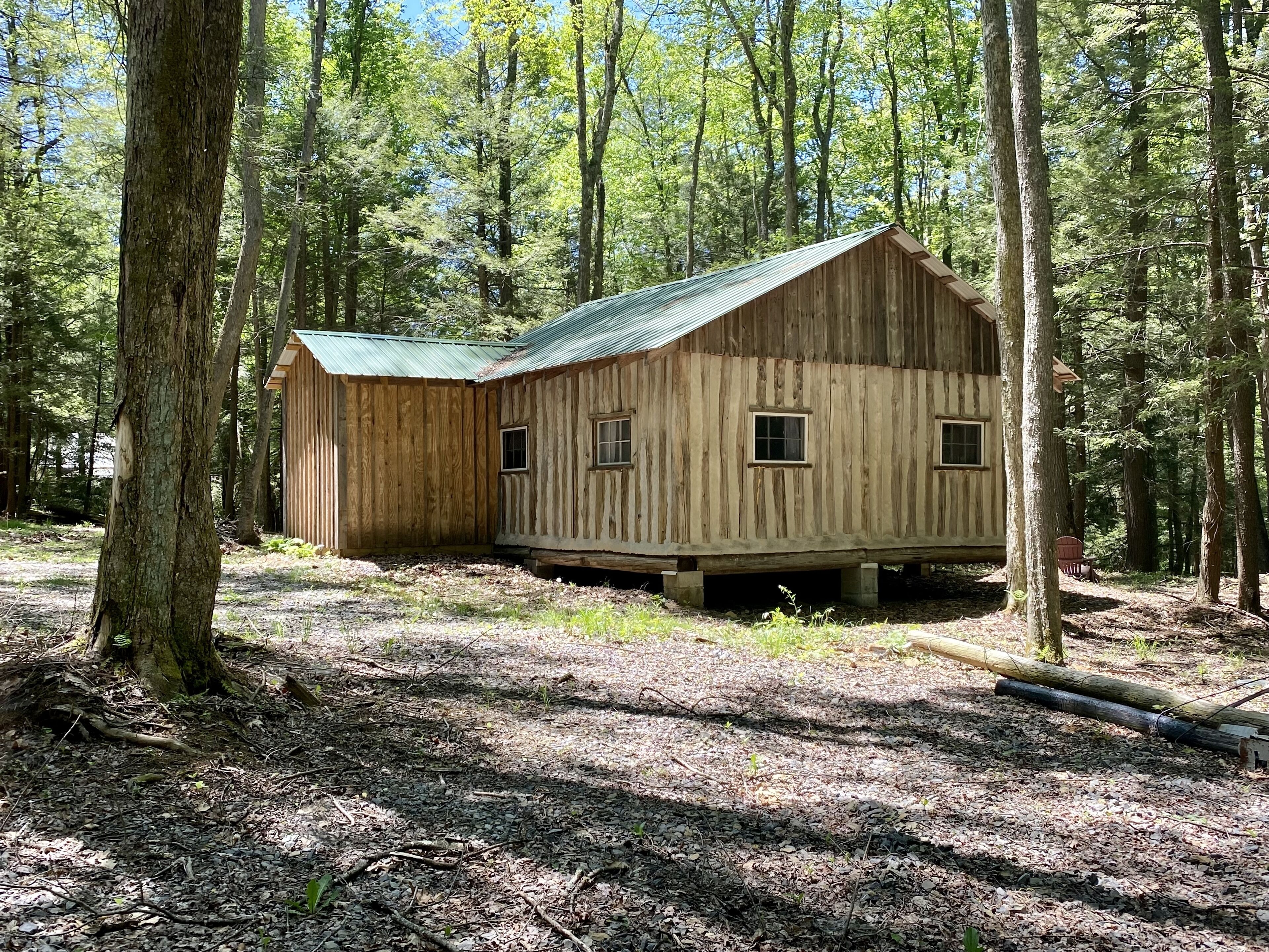 Una cabaña rústica de madera con techo inclinado, rodeada de un bosque.