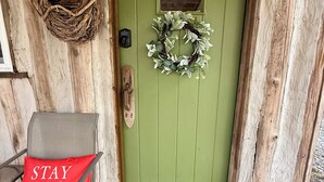 Une porte verte ornée d’une guirlande, un coussin sur lequel est brodé le mot « RESTEZ » et un paillasson avec l’inscription « BIENVENUE » sur un porche en bois.