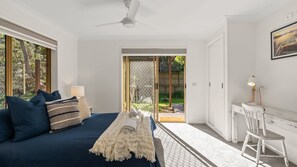 A bedroom with a bed, a desk, and a chair. There is a window and a door leading to an outdoor area.