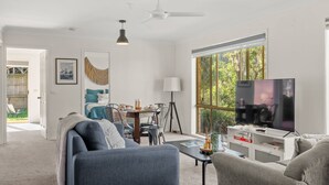 A modern living room with a sofa, TV, and dining area. - Coastal Sounds at Mollymook (Mollymook Beach)