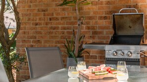 An outdoor dining area with a brick wall, a grill, and a table with glasses and watermelon slices.