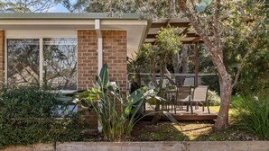 A modern house with a brick wall, large windows, and a wooden deck with chairs. - Coastal Sounds at Mollymook (Mollymook Beach)