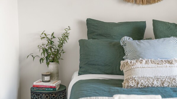 A neatly made bed with green bedding, a striped pillow, and a small plant in a white vase on a side table.