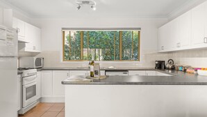 A modern kitchen with white cabinetry, a large window, and a central island. - Coastal Sounds at Mollymook (Mollymook Beach)