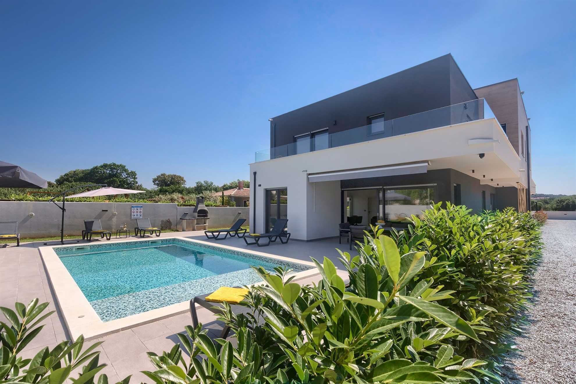 Una moderna casa a due piani con piscina, area relax all'aperto e vista sul paesaggio circostante.