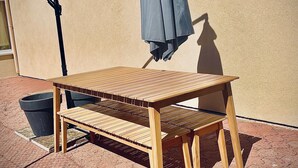 A wooden table and bench set against a beige wall, with a grey umbrella hanging above. - House near nogent sur Seine (Crancey)