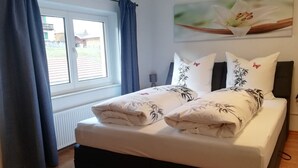Un lit bien fait, avec une literie à motifs floraux, une fenêtre avec des rideaux et un tableau représentant une fleur accroché au mur.