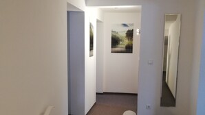 Un couloir aux murs blancs, doté d’un sol recouvert de moquette et d’une porte ornée d’un tableau représentant un paysage.