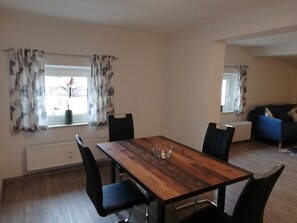 Un coin repas avec une table en bois et des chaises noires, une fenêtre avec des rideaux et un coin salon avec un canapé bleu.