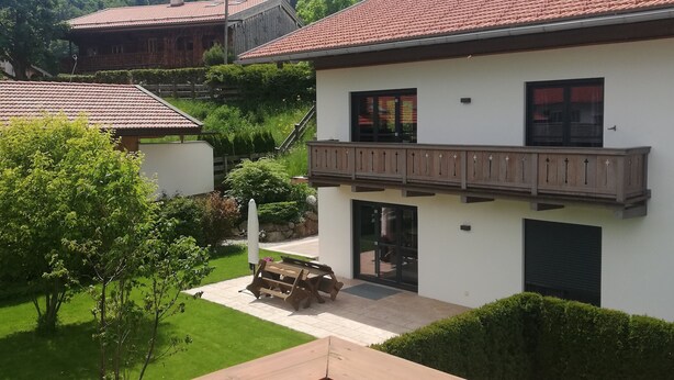 Une maison à deux étages dotée d’un balcon, d’une pelouse bien entretenue et surplombant un paysage montagneux.