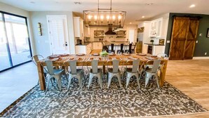 A dining area with a large table, chairs, a chandelier, and a patterned rug.
