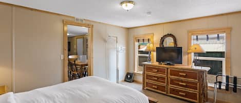 A bedroom with a bed, dresser, TV, and a window with blinds.