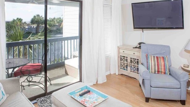 Un salon avec un balcon, une télévision, un canapé, un fauteuil et une petite table.