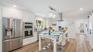 Eine moderne Küche mit Edelstahlgeräten, einer zentralen Kochinsel inklusive Barhocker und Blick ins Freie.