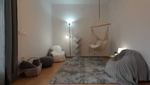 Quarto aconchegante com tapete cinza, cadeira suspensa, luminária de ch ão e pequena mesa com uma planta.