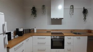 Uma cozinha com armários brancos, bancada de madeira, forno embutido, lava-louças, micro-ondas, cafeteira e plantas penduradas.