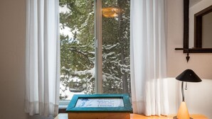 En inramad citattavla står på ett träbord nära ett fönster med vita gardiner. Bredvid finns en lampa och utsikten visar snötäckta träd.