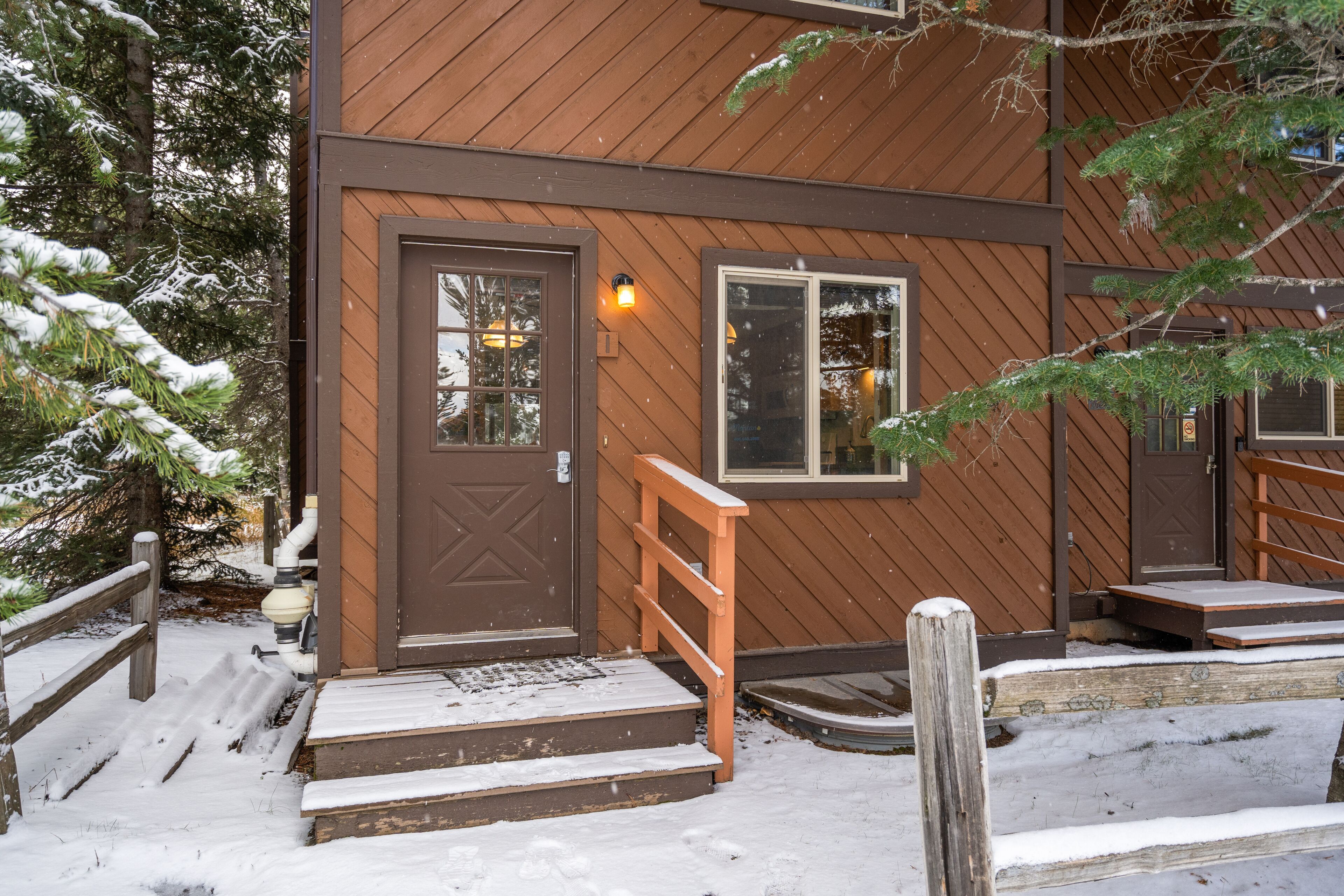 Un edificio de madera con puerta y ventanas marrones, una rampa de madera y suelo cubierto de nieve.