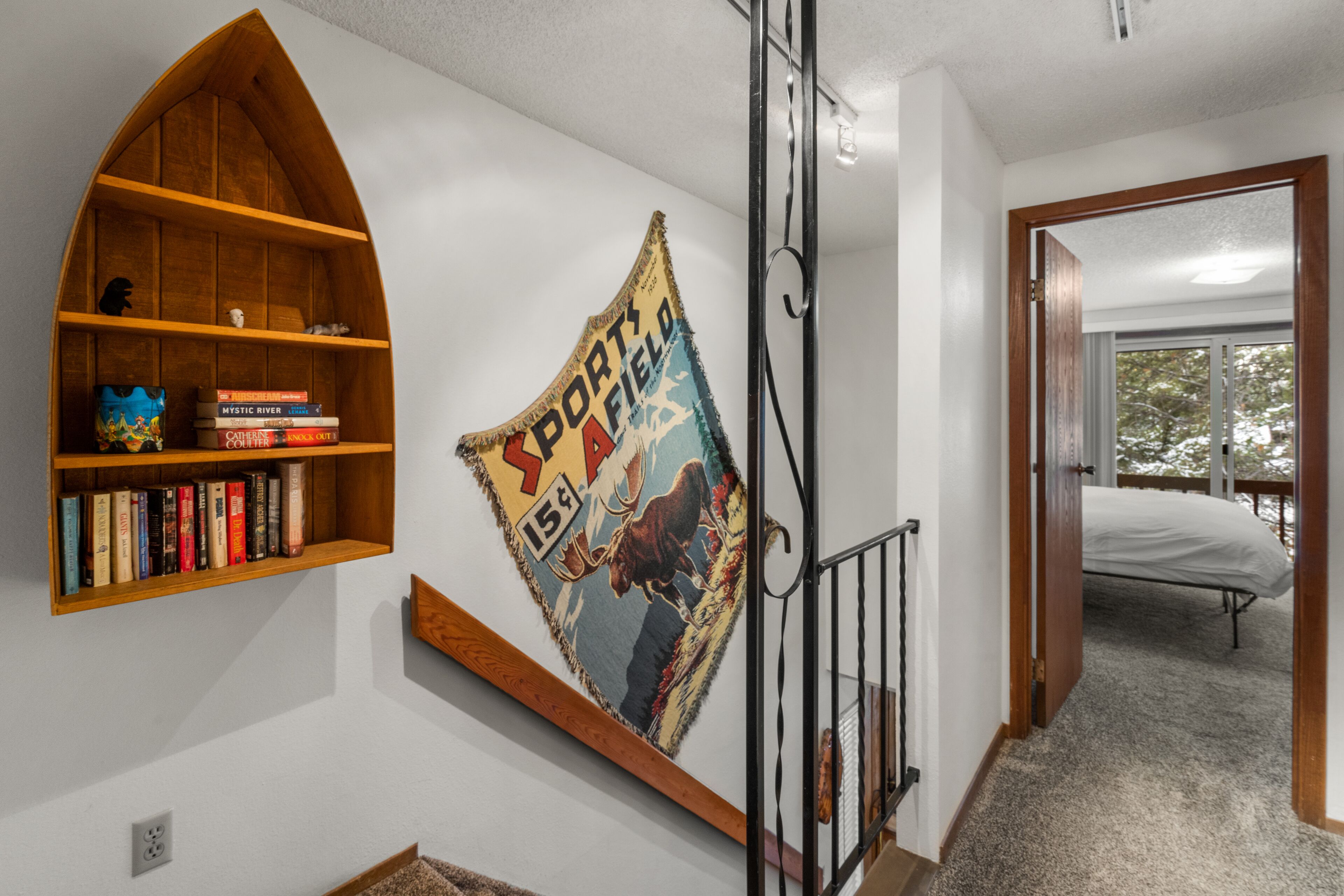 A staircase with a wooden railing, a bookshelf with books, and a flag on the wall.