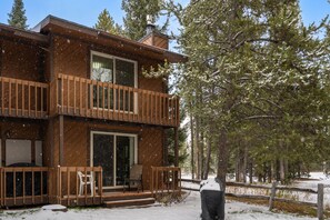 A two-story wooden cabin with a balcony, surrounded by snow-covered trees. - Homestead 1 (West Yellowstone)