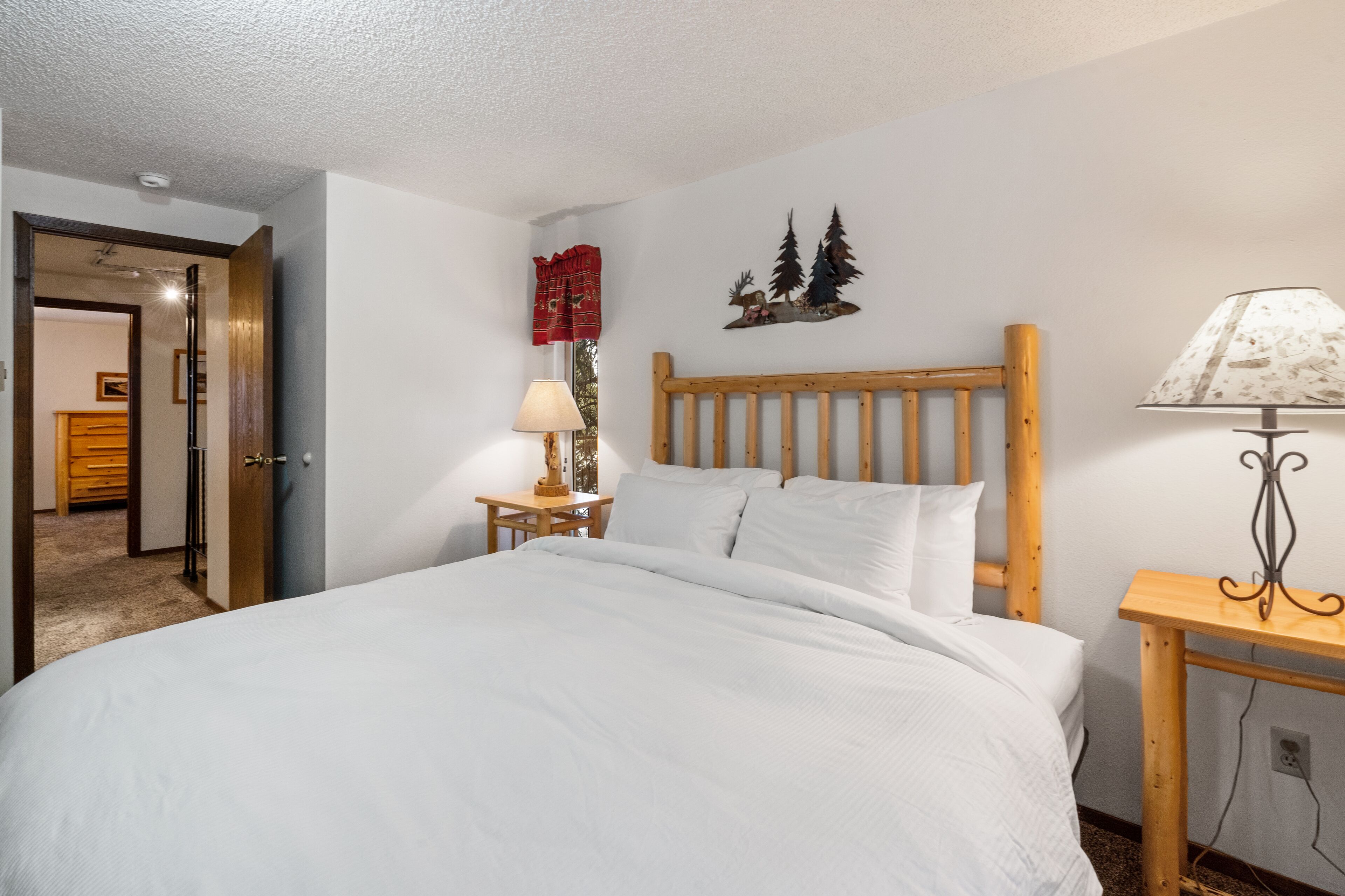 A bedroom with a wooden headboard, a bedside table with a lamp, and a wall decoration of trees.