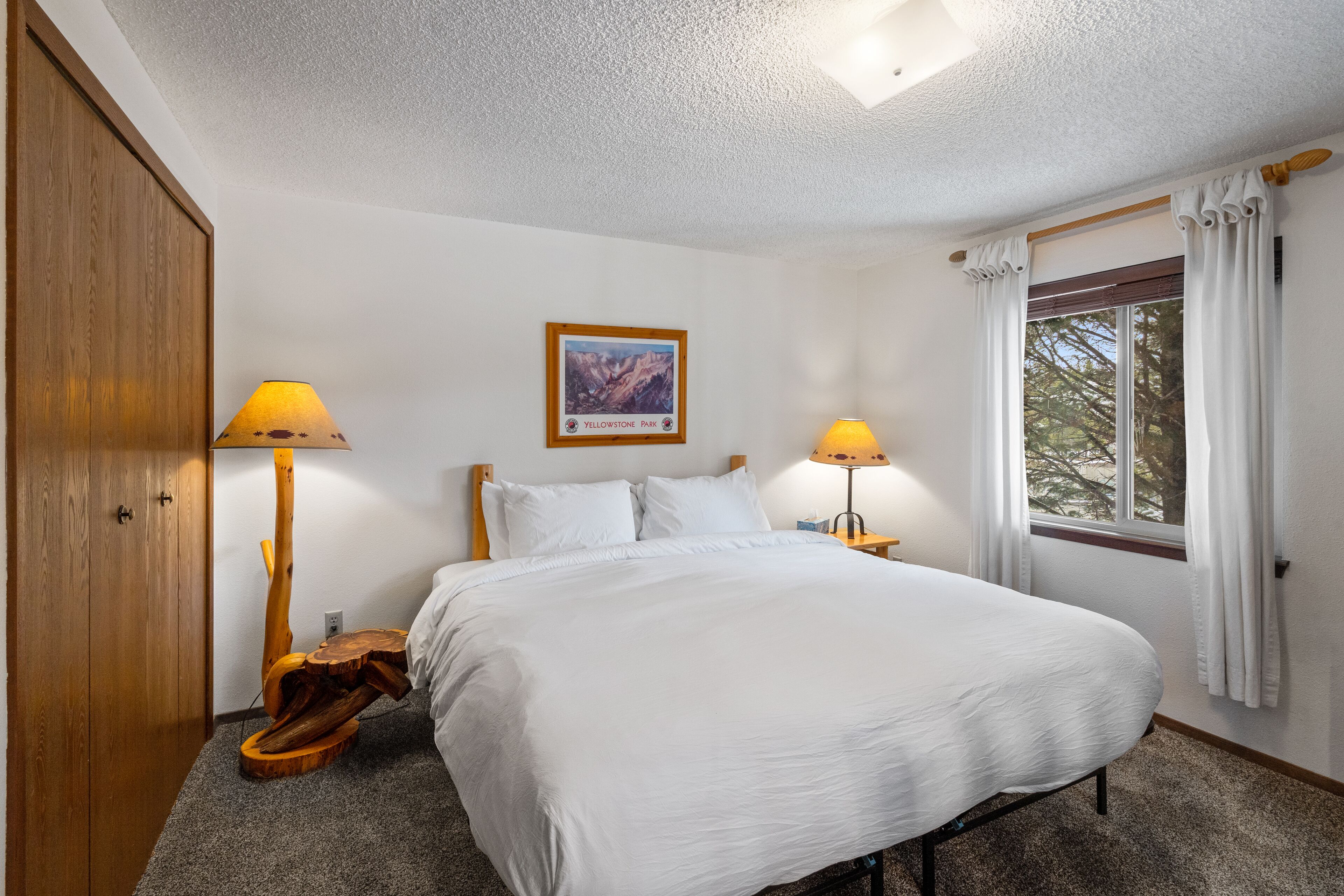 A bedroom with a large bed, two bedside lamps, a wooden cabinet, and a window with curtains.