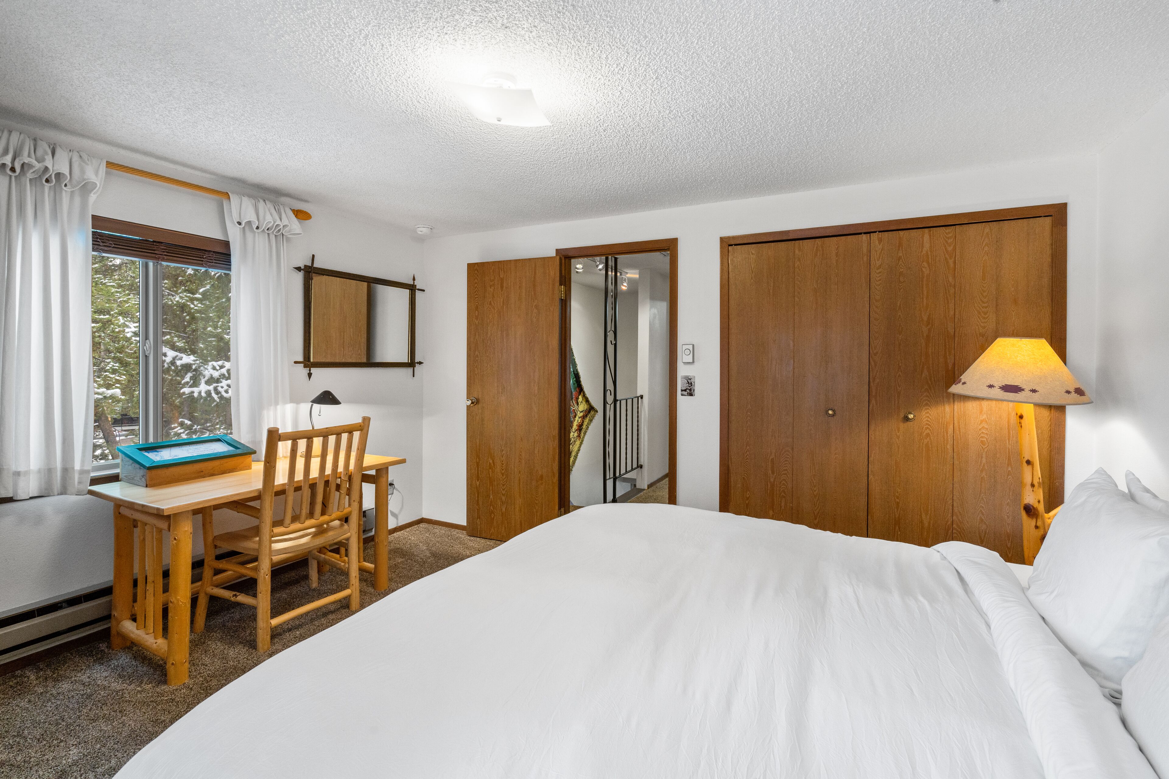 A bedroom with a bed, a desk with a chair, a lamp, and a wardrobe.