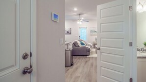 Un pasillo que conduce a un dormitorio con cama, un baño con lavamanos y espejo, y un ventilador de techo.