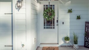 Una puerta blanca con un panel de vidrio, felpudo y planta en maceta, con un cartel que dice 'Welcome to our HOME'.