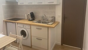 A compact kitchenette with a washing machine, a coffee maker, and a sink.