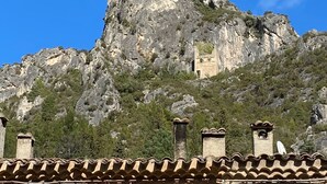 A stone building with a tiled roof, a window with a metal grille, and a chimney.