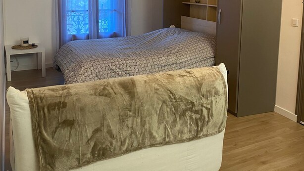 A bedroom with a bed, a wardrobe, a TV, and a window with curtains.