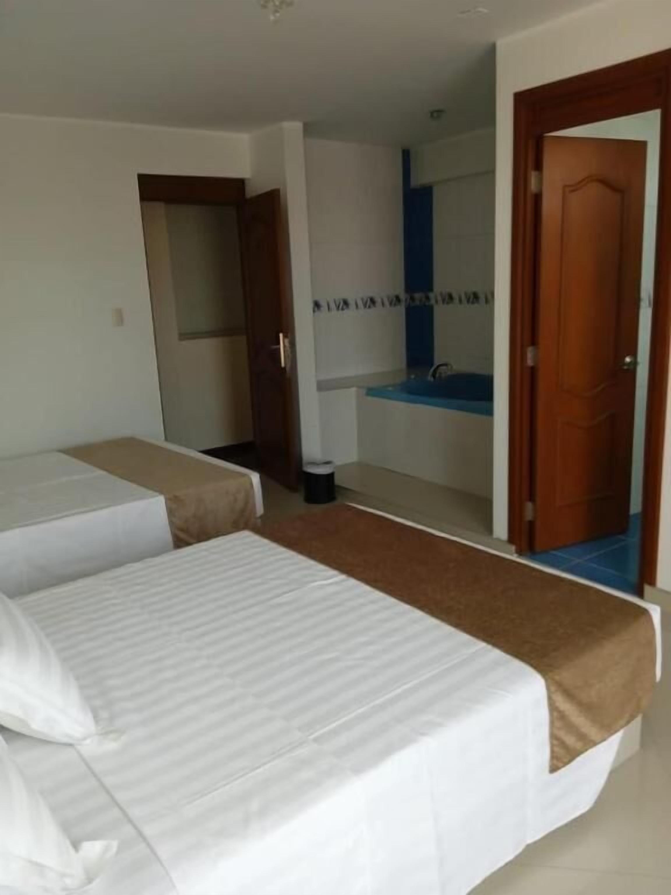 A hotel room with two single beds, a bathroom with a sink and mirror, and a door leading to another room.