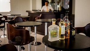 Un área de bar con una mesa redonda mostrando botellas de licores, una barra y una persona al fondo.