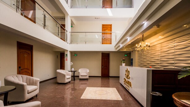 Un vestíbulo de hotel con mostrador de recepción, zona de estar y barandilla de vidrio en un nivel superior.