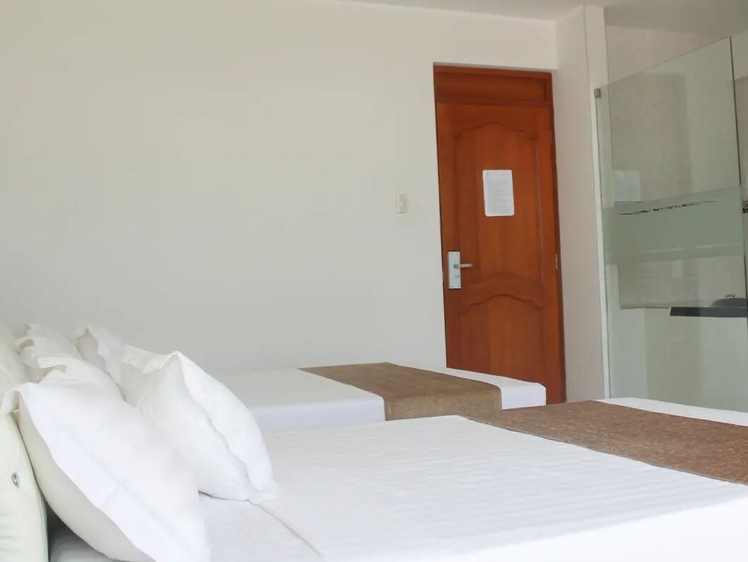 A hotel room with two single beds, a wooden door, and a glass shower enclosure.