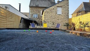 A stone building with a sloped roof, a wooden fence, and a gravel area with colorful balls. - Le Biardais - Gites du Bessin (Balleroy-sur-Drôme)