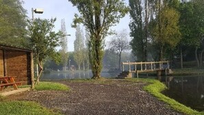 A gravel path leading to a wooden bench and a small shed, with a wooden bridge over a calm body of water. - Le Biardais - Gites du Bessin (Balleroy-sur-Drôme)