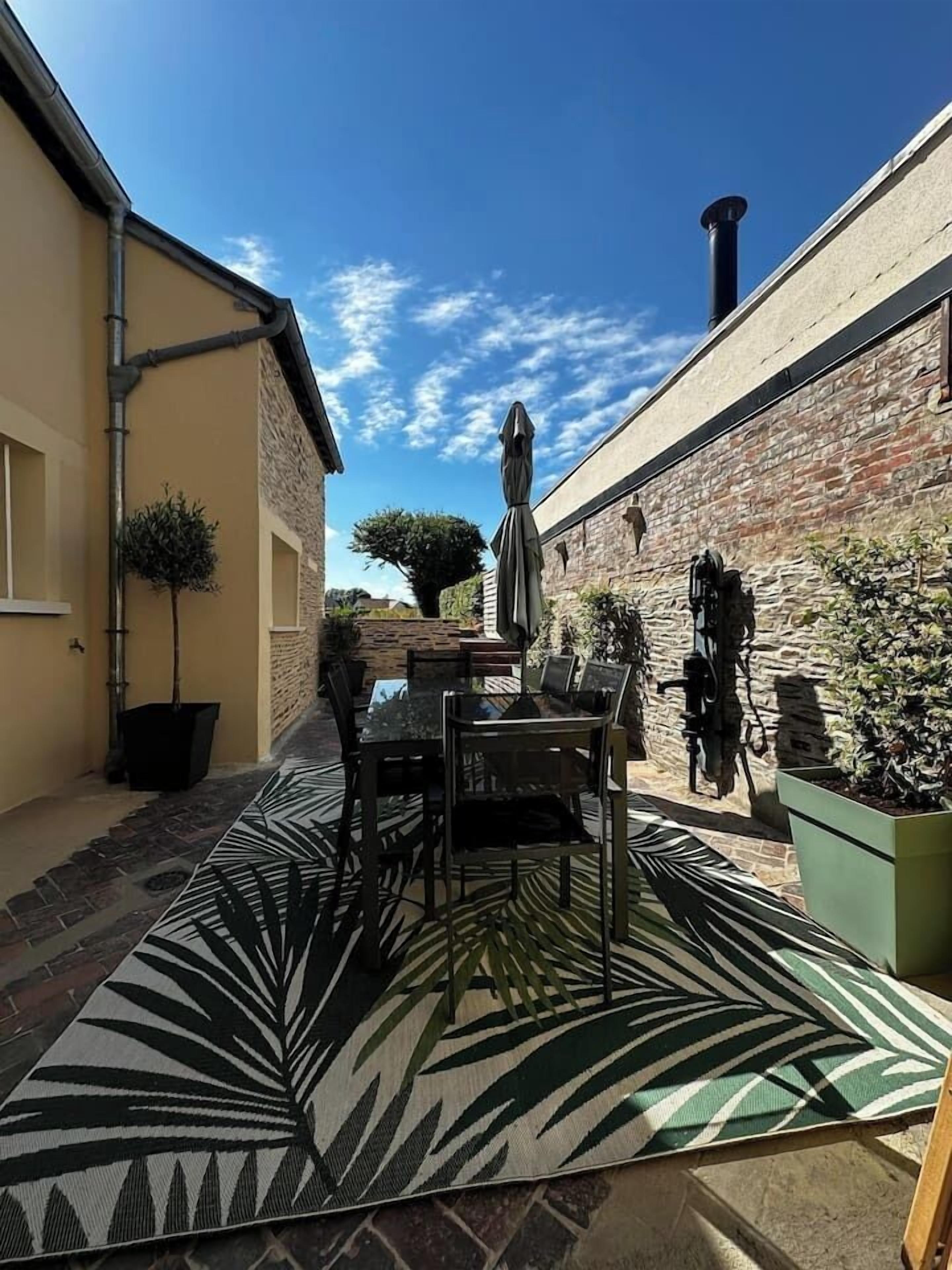 An outdoor patio with a table and chairs, a patterned rug, and potted plants.